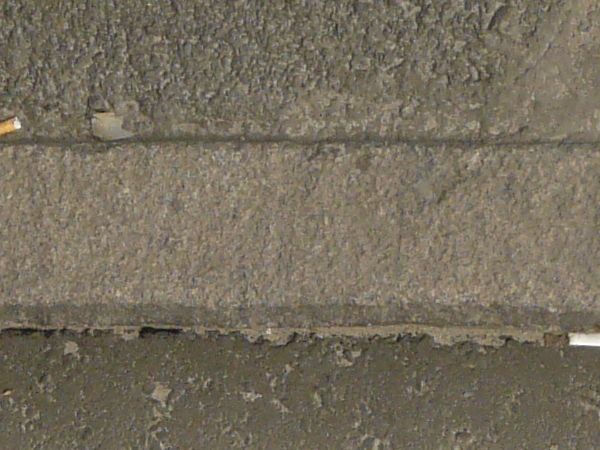 Road edge texture, dark grey in color and of varying degrees of roughness, separated in the center by a stone divider. Small amounts of grass and debris are present.